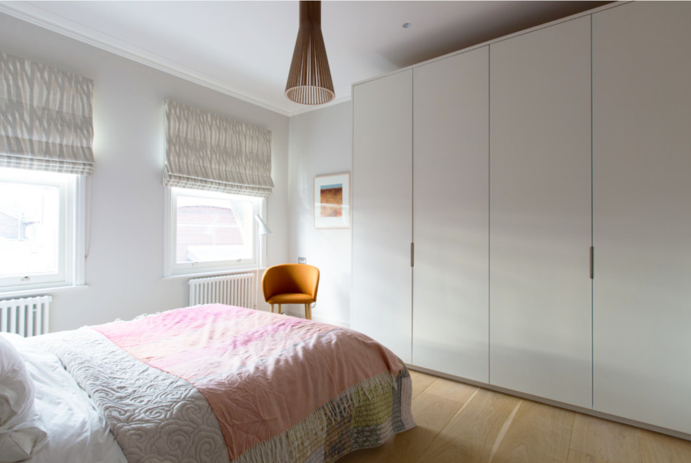 This is an example of a large scandi guest and grey and pink bedroom in London with grey walls and light hardwood flooring.