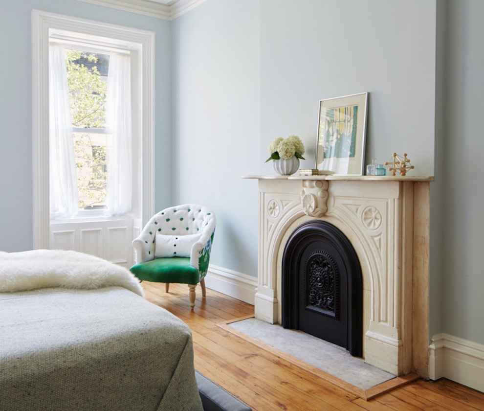 Diseño de dormitorio principal clásico renovado de tamaño medio con paredes azules, suelo de madera clara, todas las chimeneas, marco de chimenea de piedra y suelo marrón