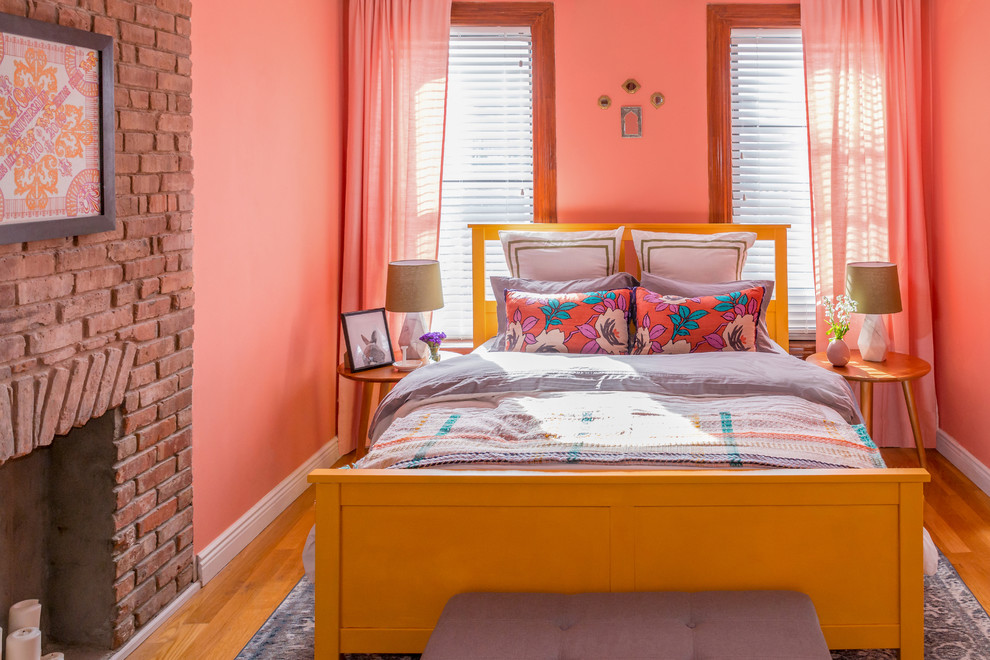 Ispirazione per una camera da letto eclettica con pareti arancioni, pavimento in legno massello medio, camino classico e cornice del camino in mattoni