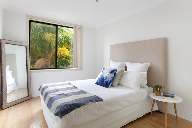 シドニーにある小さなビーチスタイルのおしゃれな客用寝室 (白い壁、淡色無垢フローリング)