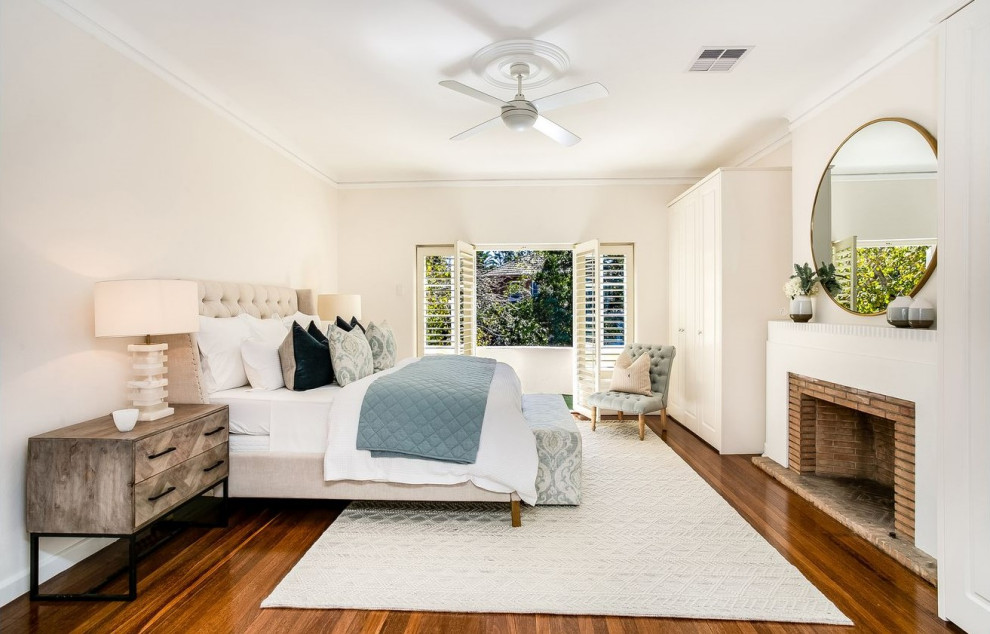 Mittelgroßes Klassisches Hauptschlafzimmer mit weißer Wandfarbe, dunklem Holzboden, Kamin, Kaminumrandung aus Backstein und braunem Boden in Sydney