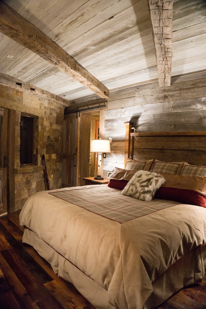Inspiration pour une chambre parentale chalet avec un sol en bois brun, une cheminée d'angle et un manteau de cheminée en pierre.