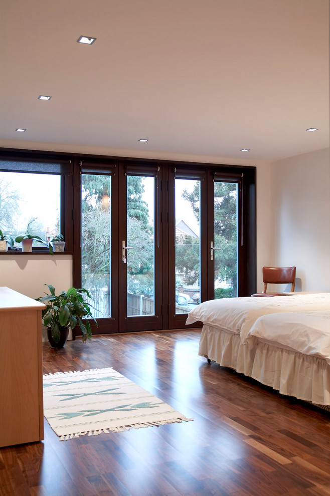 This is an example of a medium sized contemporary master bedroom in London with white walls, medium hardwood flooring, no fireplace and brown floors.