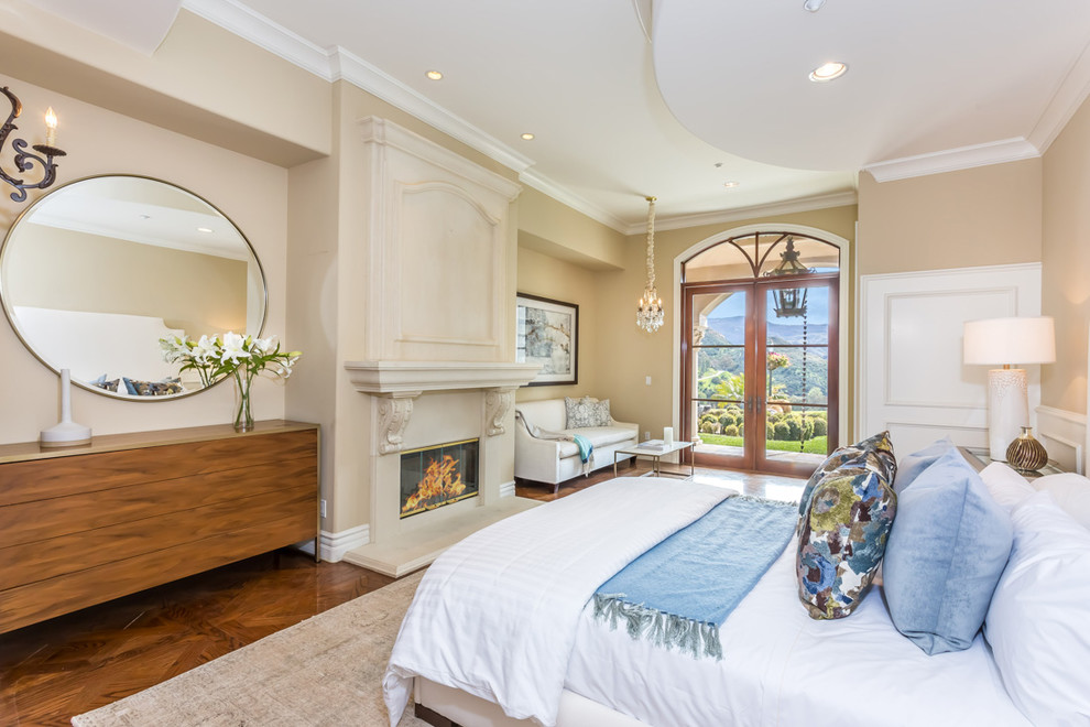 Imagen de dormitorio principal mediterráneo con paredes beige, suelo de madera en tonos medios y todas las chimeneas