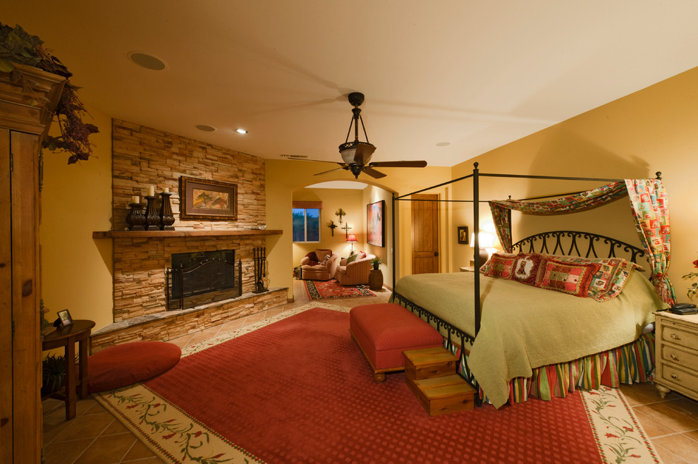 Exemple d'une chambre parentale sud-ouest américain avec un mur jaune, un sol en carrelage de céramique, une cheminée standard et un manteau de cheminée en pierre.