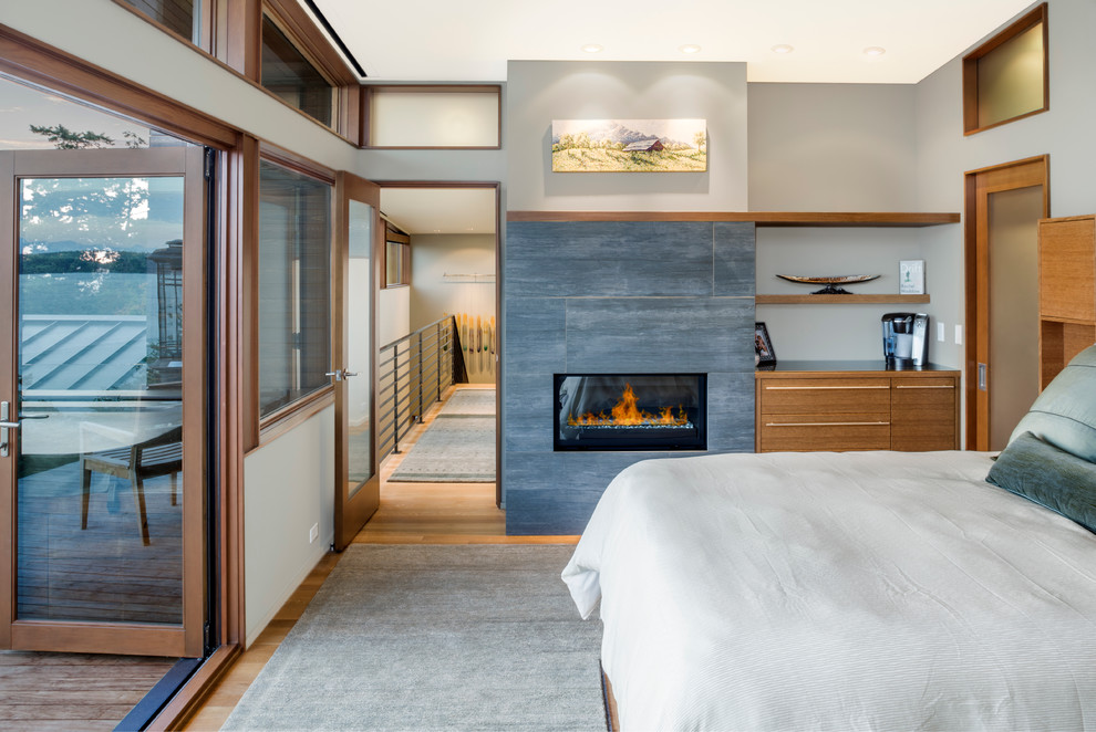 Contemporary master bedroom in Seattle with a stone fireplace surround, grey walls, light hardwood flooring and a standard fireplace.