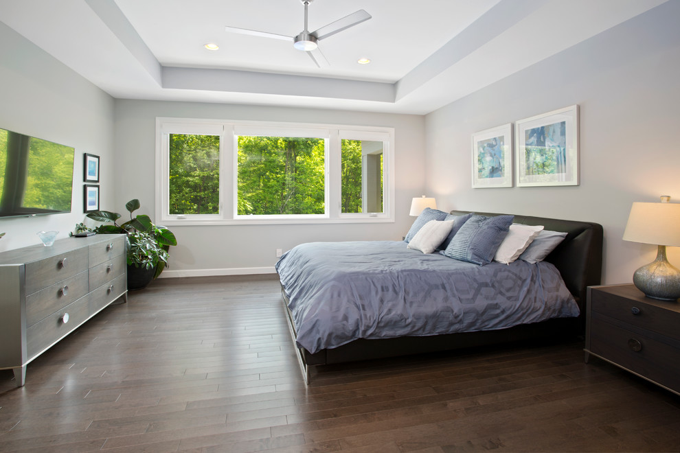 Modelo de dormitorio principal moderno grande con paredes grises y suelo de madera en tonos medios