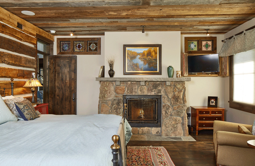 Imagen de habitación de invitados rústica grande con suelo de madera oscura, todas las chimeneas, marco de chimenea de piedra y paredes blancas