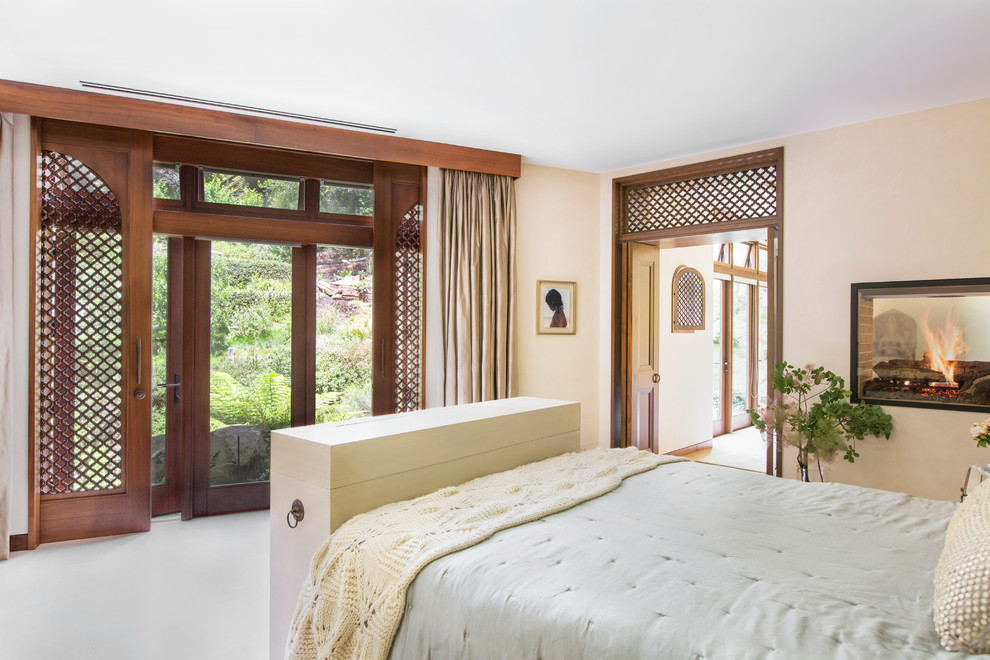 Пример оригинального дизайна: большая хозяйская спальня в стиле неоклассика (современная классика) с бежевыми стенами, ковровым покрытием, двусторонним камином и фасадом камина из штукатурки