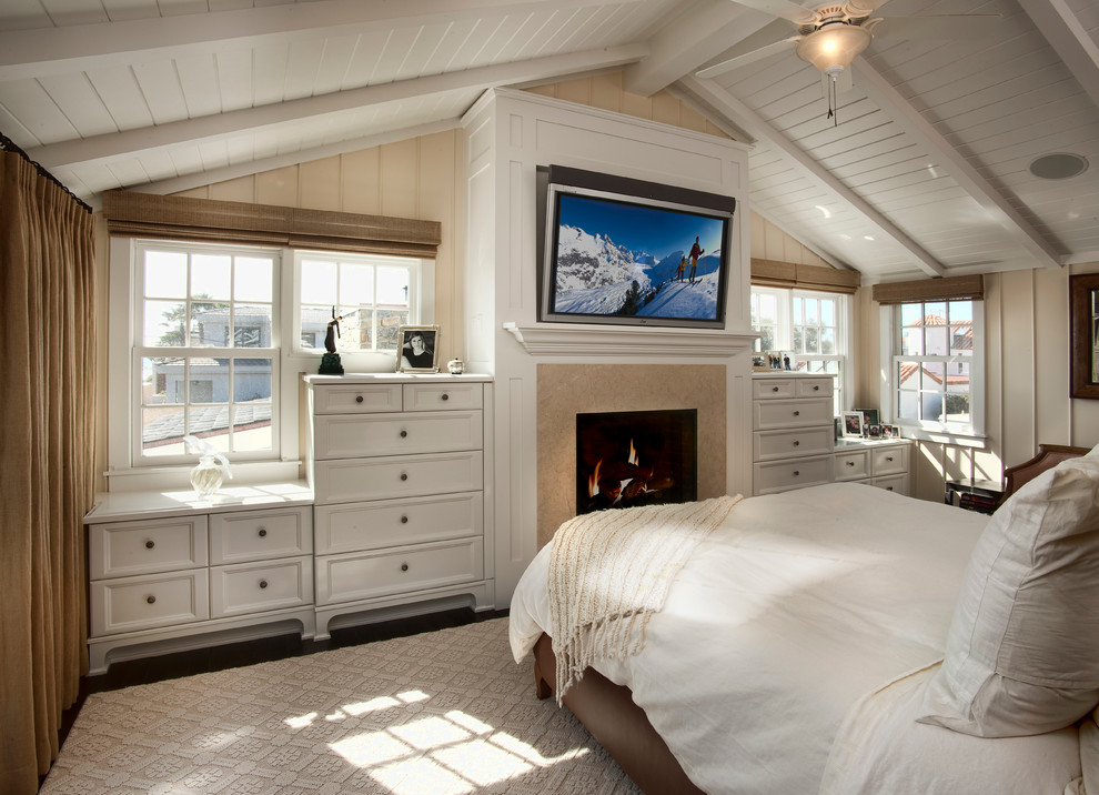 Maritimes Hauptschlafzimmer mit Kamin, beiger Wandfarbe, dunklem Holzboden und Kaminumrandung aus Stein in San Diego