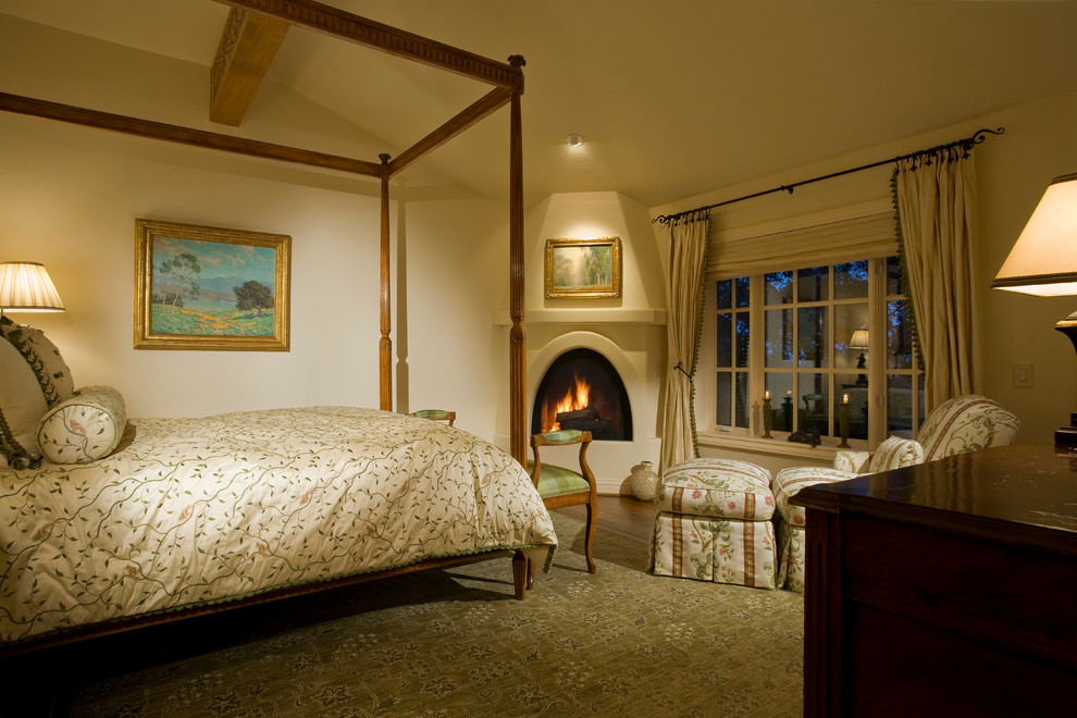 Aménagement d'une petite chambre parentale classique avec un mur beige, un sol en bois brun, une cheminée d'angle et un manteau de cheminée en plâtre.
