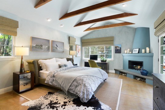 ロサンゼルスにある広い地中海スタイルのおしゃれな主寝室 (青い壁、コンクリートの床、コーナー設置型暖炉、漆喰の暖炉まわり、茶色い床)