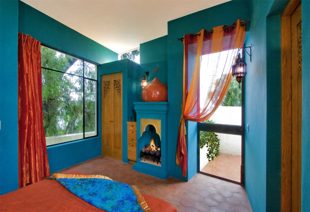 メキシコシティにあるサンタフェスタイルのおしゃれな寝室 (青い壁、テラコッタタイルの床、標準型暖炉、赤い床) のインテリア
