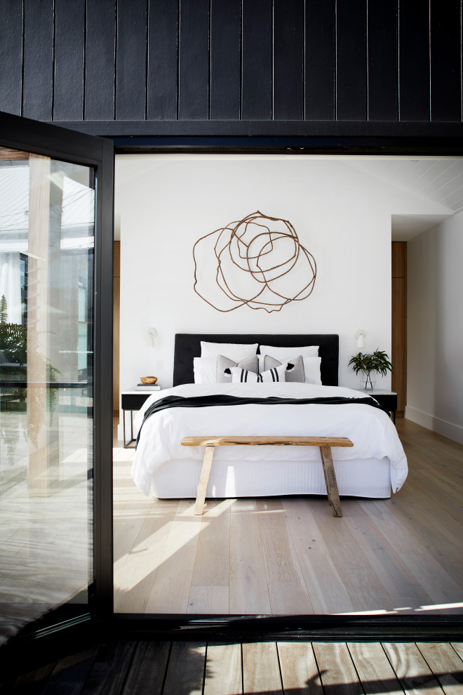 Foto de dormitorio principal minimalista de tamaño medio con paredes blancas, suelo de madera clara, chimenea de doble cara, marco de chimenea de yeso y suelo beige