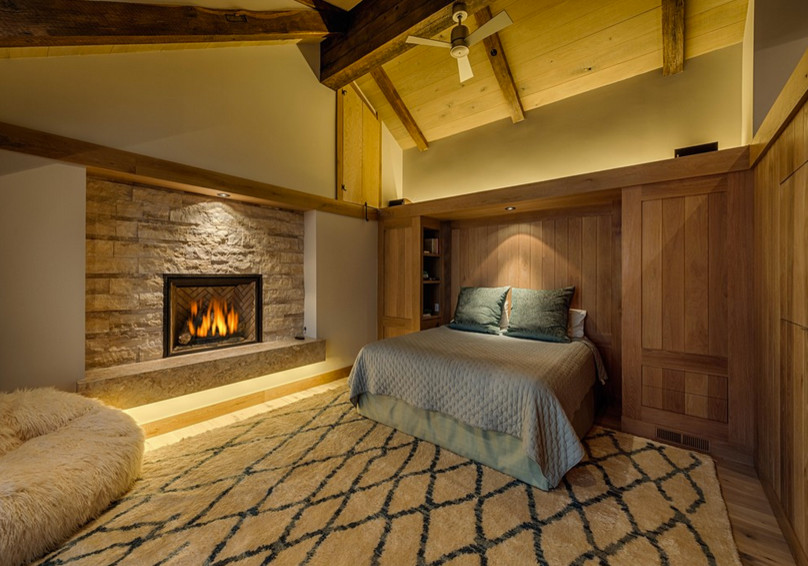 Idée de décoration pour une grande chambre parentale chalet avec un mur beige, parquet clair, une cheminée standard et un manteau de cheminée en pierre.