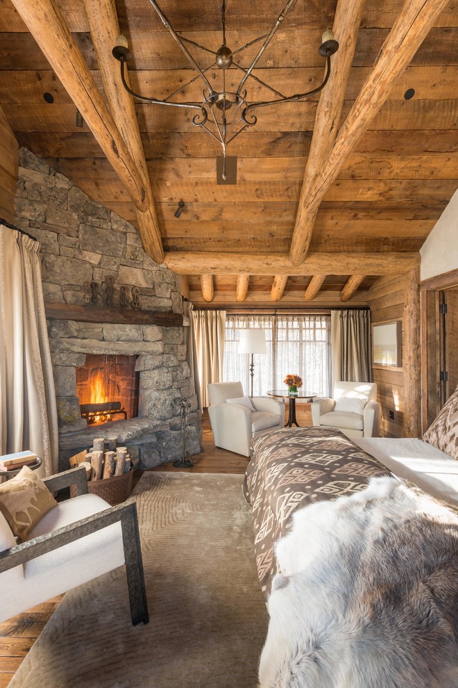 Cette image montre une chambre chalet avec un mur beige, un sol en bois brun, une cheminée d'angle et un manteau de cheminée en pierre.