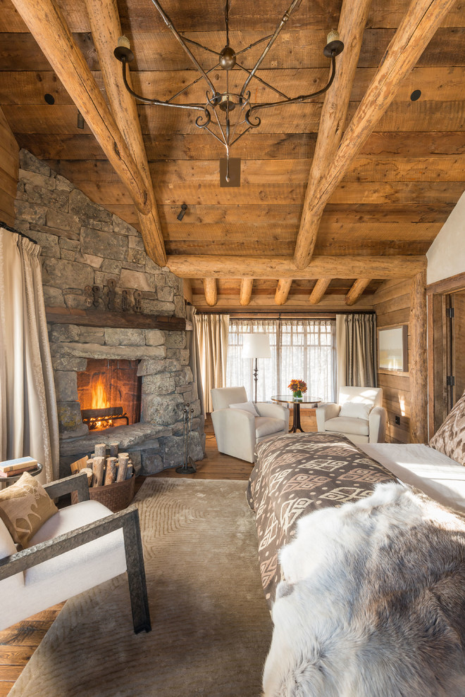 Ejemplo de dormitorio principal rural con suelo de madera en tonos medios, marco de chimenea de piedra y chimenea de esquina