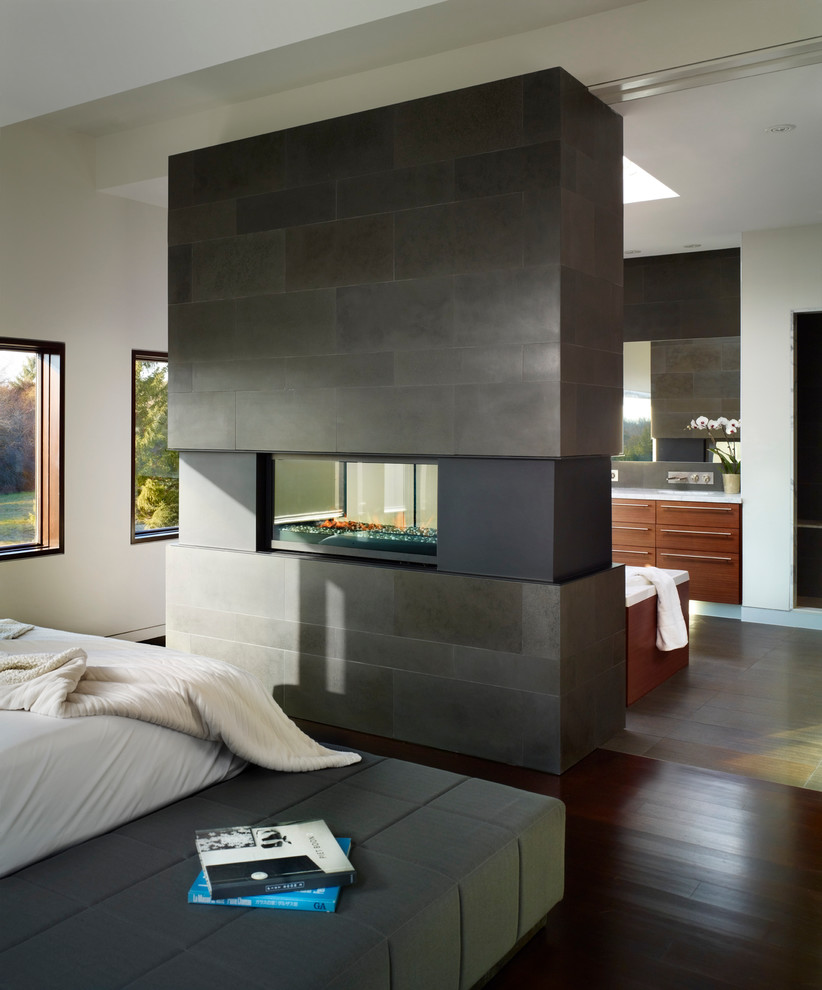 Источник вдохновения для домашнего уюта: хозяйская спальня среднего размера в современном стиле с двусторонним камином, белыми стенами, темным паркетным полом, фасадом камина из камня и коричневым полом