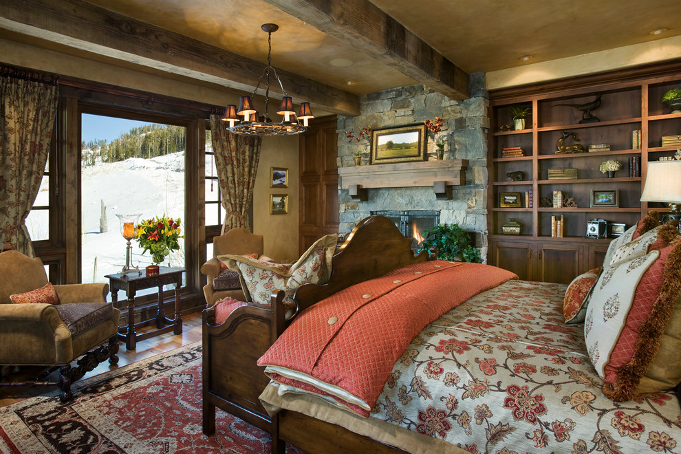 Diseño de dormitorio rústico con paredes beige, suelo de madera en tonos medios, todas las chimeneas y marco de chimenea de piedra