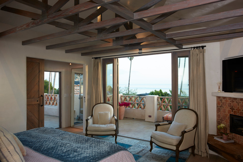 サンルイスオビスポにある中くらいなビーチスタイルのおしゃれな主寝室 (ベージュの壁、淡色無垢フローリング、コーナー設置型暖炉、タイルの暖炉まわり、茶色い床) のインテリア