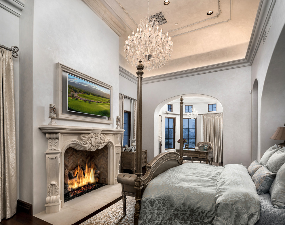 Imagen de dormitorio principal romántico extra grande con paredes grises, suelo de madera oscura, todas las chimeneas, marco de chimenea de piedra y suelo marrón