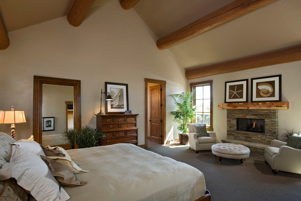 Large mountain style master carpeted bedroom photo in Other with beige walls, a standard fireplace and a stone fireplace
