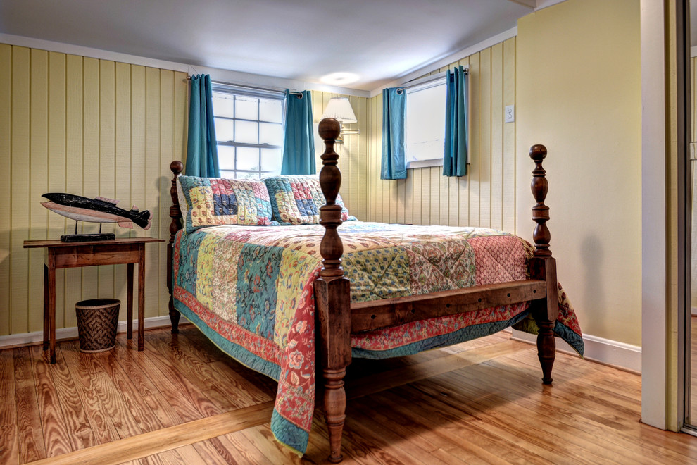 Modelo de habitación de invitados costera de tamaño medio sin chimenea con paredes amarillas, suelo de madera en tonos medios y suelo marrón