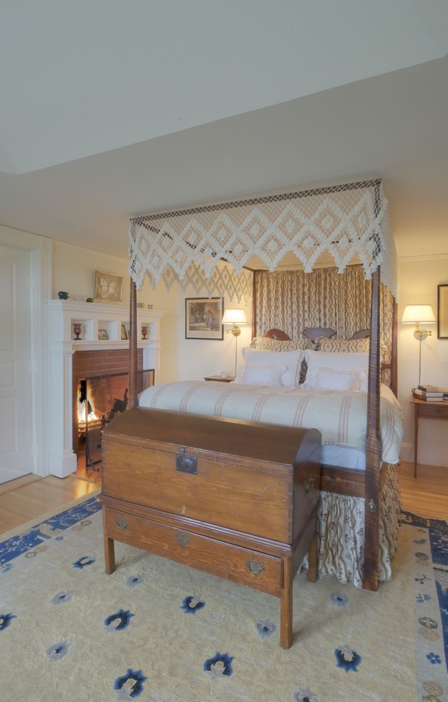 Modelo de dormitorio tradicional con paredes beige, suelo de madera en tonos medios, todas las chimeneas y marco de chimenea de ladrillo