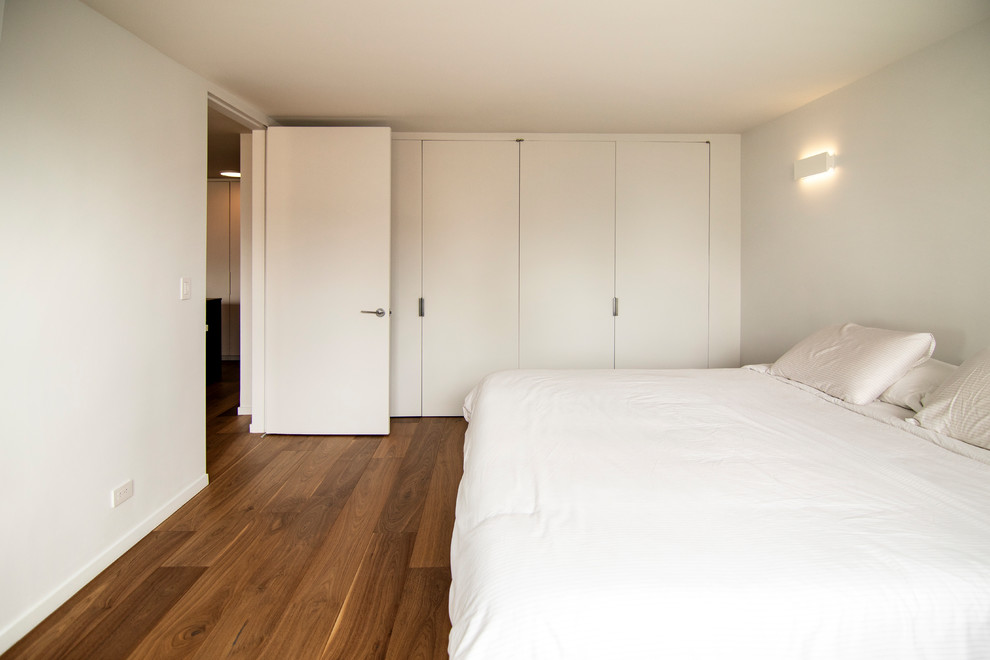 Idée de décoration pour une chambre parentale minimaliste de taille moyenne avec un mur blanc, un sol en bois brun et un sol marron.
