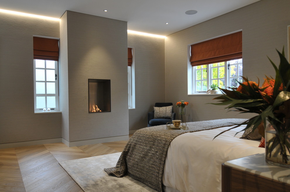 Стильный дизайн: хозяйская спальня среднего размера в современном стиле с серыми стенами, паркетным полом среднего тона, горизонтальным камином и фасадом камина из металла - последний тренд