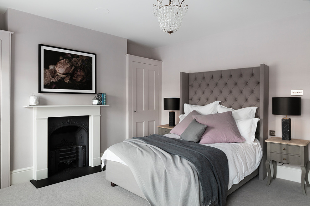 Photo of a medium sized traditional guest and grey and pink bedroom in London with grey walls, carpet, a standard fireplace, a stone fireplace surround and grey floors.