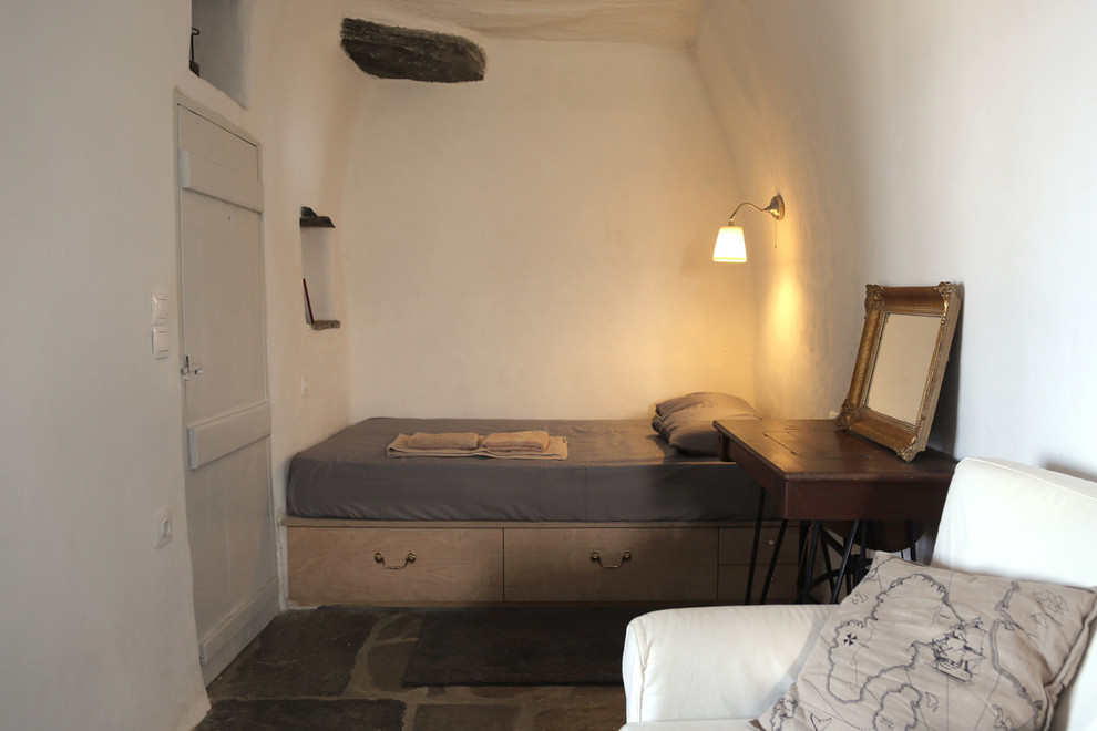 Inspiration för ett litet medelhavsstil sovrum, med vita väggar, skiffergolv och en spiselkrans i sten