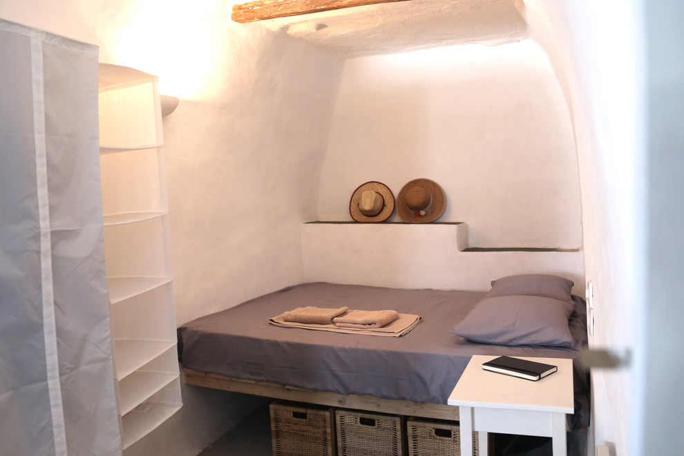 Imagen de dormitorio mediterráneo pequeño con paredes blancas y marco de chimenea de piedra
