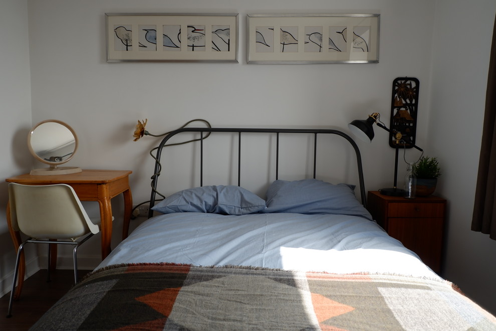 Ejemplo de habitación de invitados actual pequeña con paredes blancas, suelo laminado y suelo marrón