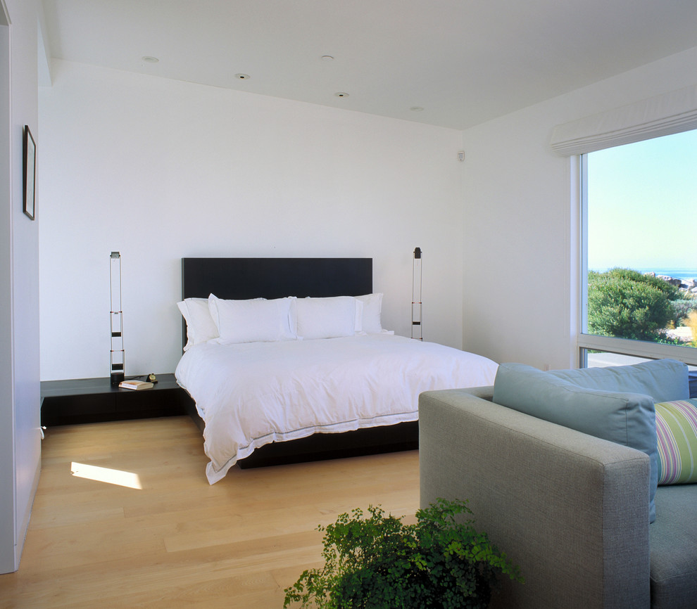 Diseño de dormitorio costero sin chimenea con paredes blancas y suelo de madera clara