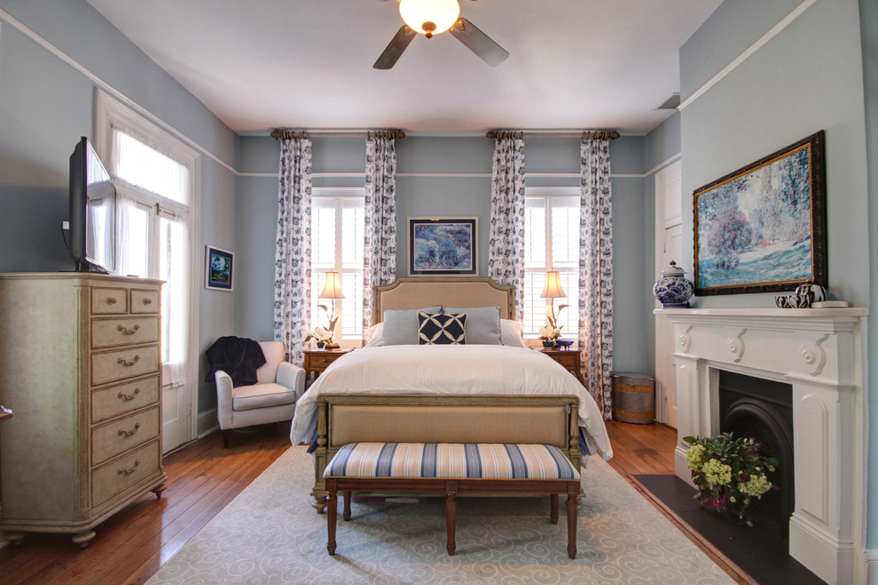 Mittelgroßes Klassisches Hauptschlafzimmer mit blauer Wandfarbe, braunem Holzboden, Kamin, Kaminumrandung aus Holz und braunem Boden in Charleston