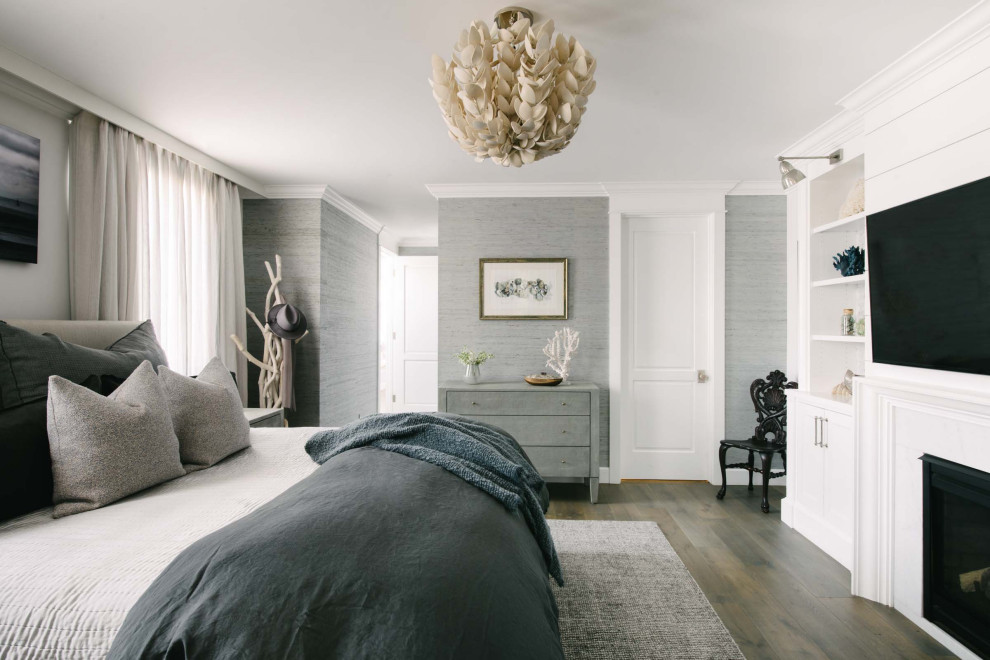 Inspiration for a beach style grey and brown bedroom in Los Angeles with grey walls, dark hardwood flooring, a standard fireplace, brown floors and wallpapered walls.
