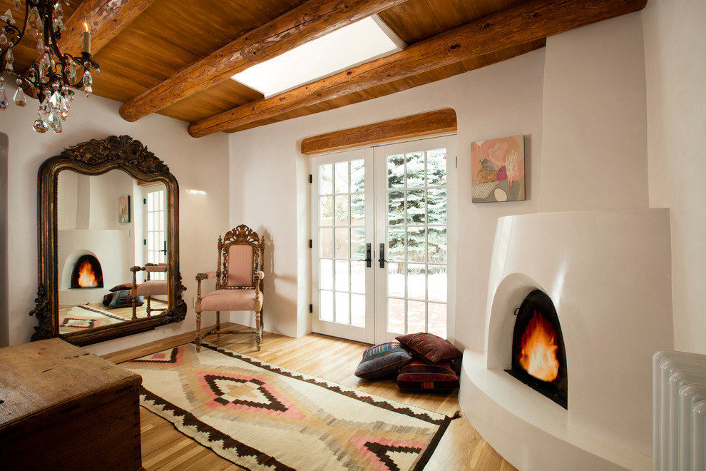 Foto de dormitorio principal de estilo americano de tamaño medio con paredes blancas, suelo de madera clara, chimenea de esquina y marco de chimenea de yeso