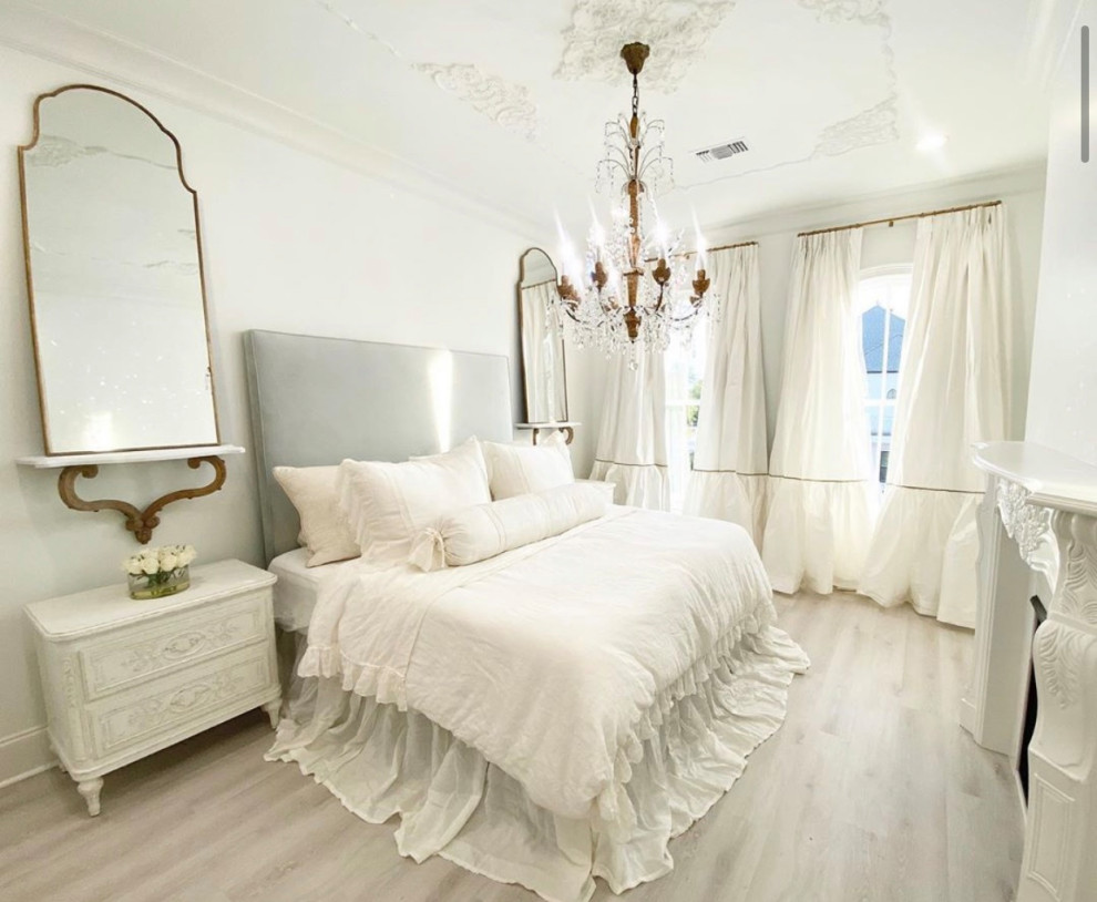 Diseño de dormitorio principal con paredes blancas, suelo de madera clara, marco de chimenea de madera y suelo beige