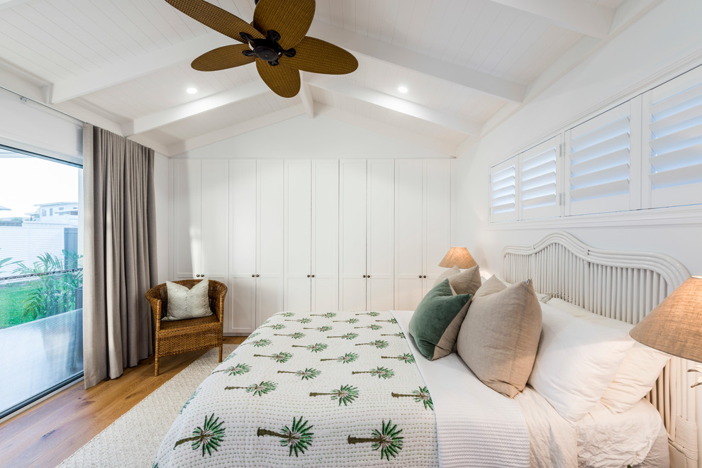 Diseño de dormitorio principal costero grande con paredes blancas, suelo de madera en tonos medios y suelo marrón