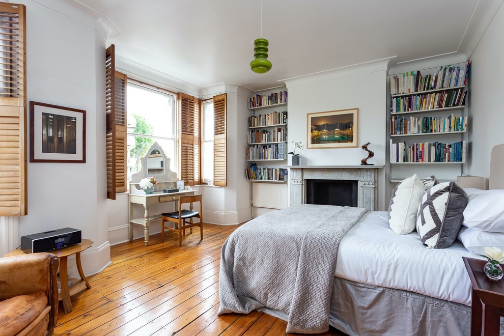 Imagen de dormitorio clásico renovado con paredes blancas, suelo de madera en tonos medios, todas las chimeneas, marco de chimenea de piedra y suelo marrón