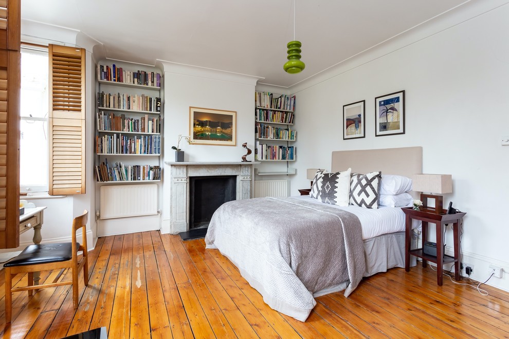 Mid-Century Schlafzimmer mit weißer Wandfarbe, braunem Holzboden, Kamin, Kaminumrandung aus Stein und braunem Boden in London