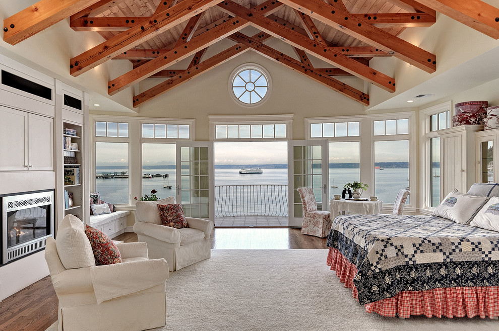 Cette photo montre une grande chambre parentale bord de mer avec un sol en bois brun, une cheminée standard, un manteau de cheminée en métal et un mur beige.