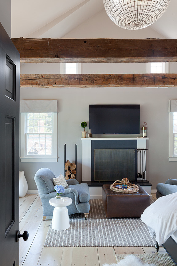 Imagen de dormitorio principal costero grande con paredes grises, suelo de madera clara, todas las chimeneas y marco de chimenea de piedra