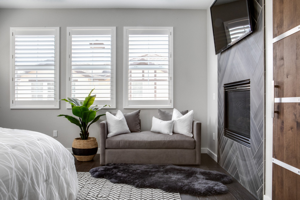 Mittelgroßes Modernes Hauptschlafzimmer mit grauer Wandfarbe, dunklem Holzboden, Kamin, gefliester Kaminumrandung und braunem Boden in Orange County