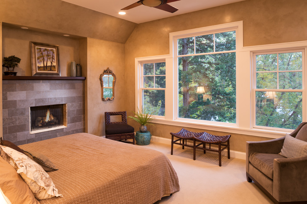Photo of a large traditional master bedroom in Minneapolis with brown walls, carpet, a standard fireplace, a tiled fireplace surround and beige floors.