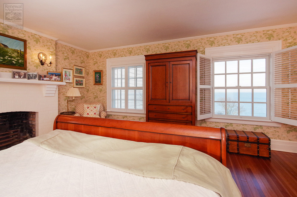 Mittelgroßes Hauptschlafzimmer mit gelber Wandfarbe, dunklem Holzboden, Kamin, Kaminumrandung aus Backstein und braunem Boden in Newark
