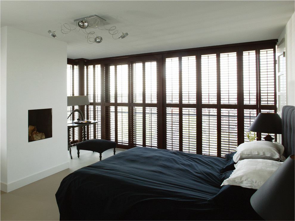 Cette photo montre une chambre chic de taille moyenne avec un mur blanc, une cheminée standard, un manteau de cheminée en plâtre et sol en béton ciré.