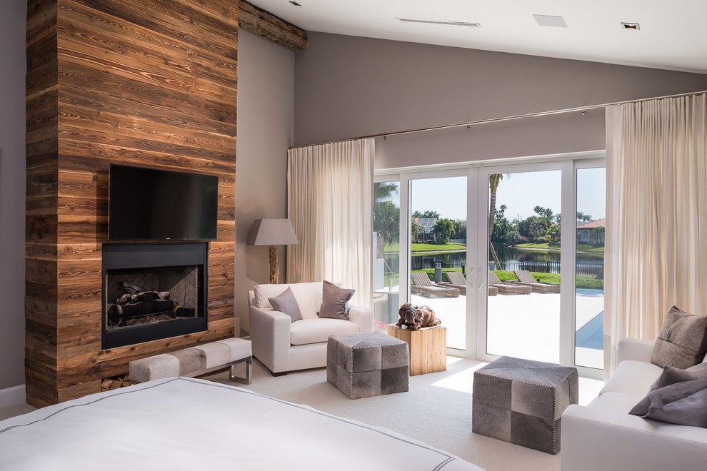 На фото: спальня в современном стиле с серыми стенами, ковровым покрытием, стандартным камином и фасадом камина из дерева с