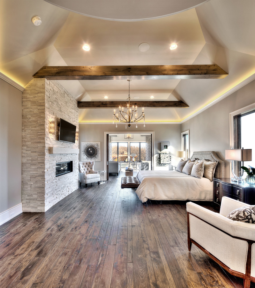 Foto de dormitorio principal actual extra grande con paredes grises, suelo de madera en tonos medios, chimenea lineal y marco de chimenea de piedra